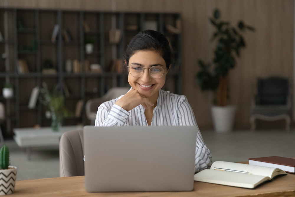 Woman in a white shirt sitting at a table and looking at her laptop
